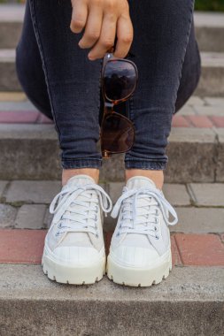 Kız merdivenlerde oturuyor ve elinde güneş gözlüğü tutuyor.