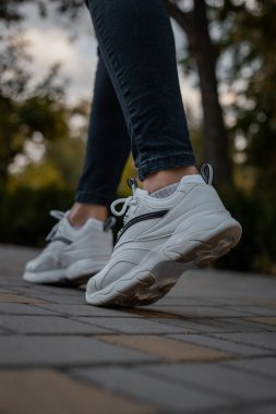 Sokakta siyah kotlu bir kızın ayağında beyaz ayakkabılar.