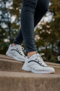 Sokakta siyah kotlu bir kızın ayağında beyaz ayakkabılar.