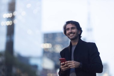 Alacakaranlıkta arka planda şehir manzarası olan akıllı telefon kullanan genç bir adam görüntüsü. Yüksek kalite fotoğraf. 