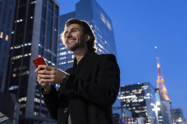 Gece vakti arka planda şehir manzarası olan akıllı telefon kullanan genç bir adamın görüntüsü. Yüksek kalite fotoğraf. 