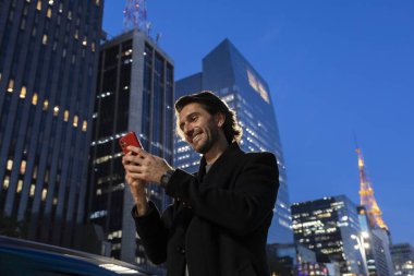 Gece vakti arka planda şehir manzarası olan akıllı telefon kullanan genç bir adamın görüntüsü. Yüksek kalite fotoğraf. 