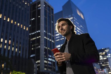 Gece vakti arka planda şehir manzarası olan akıllı telefon kullanan genç bir adamın görüntüsü. Yüksek kalite fotoğraf. 