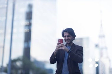 Alacakaranlıkta arka planda şehir manzarası olan akıllı telefon kullanan genç bir adam görüntüsü. Yüksek kalite fotoğraf. 