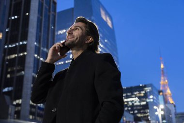 Gece vakti arka planda şehir manzarası olan akıllı telefon kullanan genç bir adamın görüntüsü. Yüksek kalite fotoğraf. 