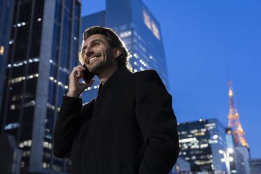 Gece vakti arka planda şehir manzarası olan akıllı telefon kullanan genç bir adamın görüntüsü. Yüksek kalite fotoğraf. 