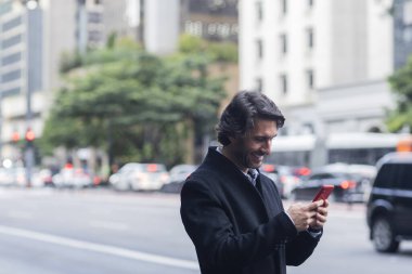 Gündüz vakti akıllı telefonlu genç adam manzarası ve arka planda şehir manzarası. Yüksek kalite fotoğraf. 