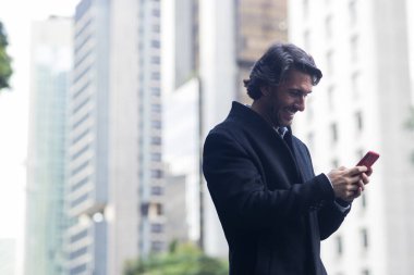 Gündüz vakti akıllı telefonlu genç adam manzarası ve arka planda şehir manzarası. Yüksek kalite fotoğraf. 