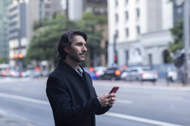 Gündüz vakti akıllı telefonlu genç adam manzarası ve arka planda şehir manzarası. Yüksek kalite fotoğraf. 