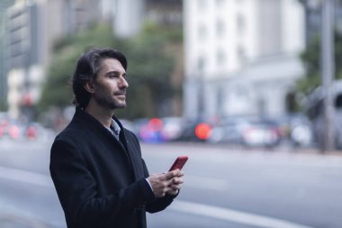 Gündüz vakti akıllı telefonlu genç adam manzarası ve arka planda şehir manzarası. Yüksek kalite fotoğraf. 