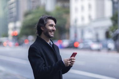 Gündüz vakti akıllı telefonlu genç adam manzarası ve arka planda şehir manzarası. Yüksek kalite fotoğraf. 