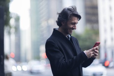 Gündüz vakti akıllı telefonlu genç adam manzarası ve arka planda şehir manzarası. Yüksek kalite fotoğraf. 