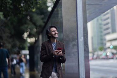 Gündüz vakti akıllı telefonlu genç adam manzarası ve arka planda şehir manzarası. Yüksek kalite fotoğraf. 