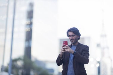 Gündüz vakti akıllı telefonlu genç adam manzarası ve arka planda şehir manzarası. Yüksek kalite fotoğraf. 