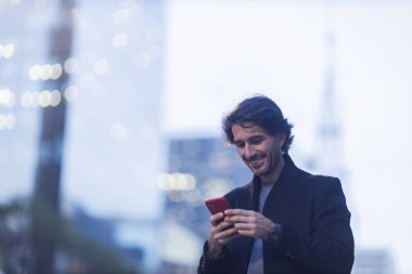 Alacakaranlıkta akıllı telefonlu genç adam manzarası ve arka planda şehir manzarası. Yüksek kalite fotoğraf. 