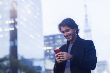 Alacakaranlıkta akıllı telefonlu genç adam manzarası ve arka planda şehir manzarası. Yüksek kalite fotoğraf. 