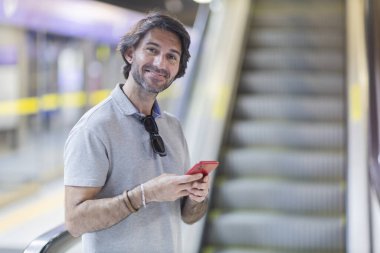 View of young man using a smartphone inside a subway - metro station with a blurred view landscape in the background. High quality photo. Texting on the phone.  clipart
