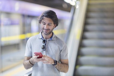 Metroda akıllı telefon kullanan genç bir adamın görüntüsü. Arka planda bulanık manzaralı metro istasyonu. Yüksek kalite fotoğraf. Telefondaki mesajlaşma.. 