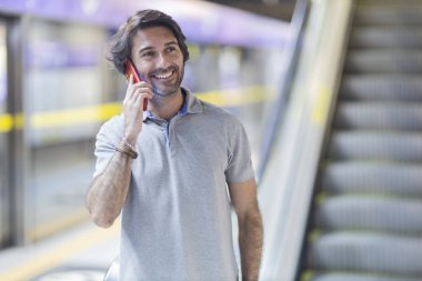 Metroda akıllı telefon kullanan genç bir adamın görüntüsü. Arka planda bulanık manzaralı metro istasyonu. Yüksek kalite fotoğraf. Telefonda konuşuyorlar.. 
