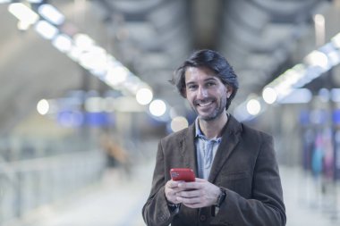 Metroda akıllı telefon kullanan genç bir adamın görüntüsü. Arka planda bulanık manzaralı metro istasyonu. Yüksek kalite fotoğraf. Telefondaki mesajlaşma.. 