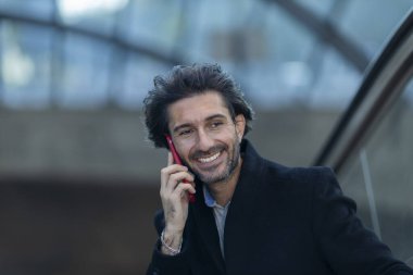 Alacakaranlıkta arka planda bulanık bir manzara olan kapalı bir alanda akıllı telefon kullanan genç bir adamın görüntüsü. Yüksek kalite fotoğraf. Telefonla konuşuyorum. Gece vakti şehir manzaralı akıllı telefon kullanan genç bir adamın görüntüsü.