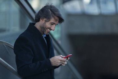 Alacakaranlıkta arka planda bulanık bir manzara olan kapalı bir alanda akıllı telefon kullanan genç bir adamın görüntüsü. Yüksek kalite fotoğraf. Telefonda mesajlaşıyoruz. Gece vakti şehir manzaralı akıllı telefon kullanan genç bir adamın görüntüsü.