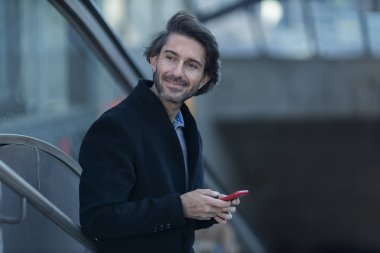 Alacakaranlıkta arka planda bulanık bir manzara olan kapalı bir alanda akıllı telefon kullanan genç bir adamın görüntüsü. Yüksek kalite fotoğraf. Telefonda mesajlaşıyoruz. Gece vakti şehir manzaralı akıllı telefon kullanan genç bir adamın görüntüsü.