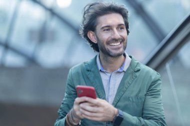 Alacakaranlıkta arka planda bulanık bir manzara olan kapalı bir alanda akıllı telefon kullanan genç bir adamın görüntüsü. Yüksek kalite fotoğraf. Telefonda mesajlaşıyoruz. Gece vakti şehir manzaralı akıllı telefon kullanan genç bir adamın görüntüsü.