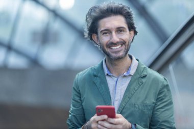 Alacakaranlıkta arka planda bulanık bir manzara olan kapalı bir alanda akıllı telefon kullanan genç bir adamın görüntüsü. Yüksek kalite fotoğraf. Telefonda mesajlaşıyoruz. Gece vakti şehir manzaralı akıllı telefon kullanan genç bir adamın görüntüsü.