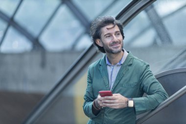 Alacakaranlıkta arka planda bulanık bir manzara olan kapalı bir alanda akıllı telefon kullanan genç bir adamın görüntüsü. Yüksek kalite fotoğraf. Telefonda mesajlaşıyoruz. Gece vakti şehir manzaralı akıllı telefon kullanan genç bir adamın görüntüsü.