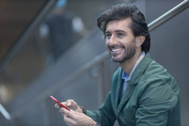 Arka planda bulanık bir manzara olan kapalı alanda akıllı telefon kullanan genç bir adamın görüntüsü. Yüksek kalite fotoğraf. Telefondaki mesajlaşma.. 