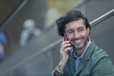 Arka planda bulanık bir manzara olan kapalı alanda akıllı telefon kullanan genç bir adamın görüntüsü. Yüksek kalite fotoğraf. Telefonda konuşuyorlar.. 