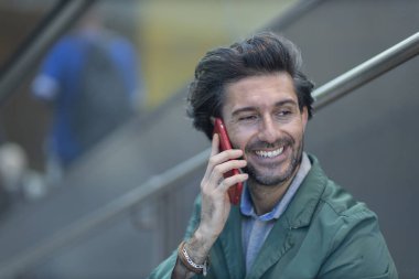 Arka planda bulanık bir manzara olan kapalı alanda akıllı telefon kullanan genç bir adamın görüntüsü. Yüksek kalite fotoğraf. Telefonda konuşuyorlar.. 