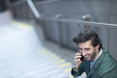 Arka planda bulanık bir manzara olan kapalı alanda akıllı telefon kullanan genç bir adamın görüntüsü. Yüksek kalite fotoğraf. Telefonda konuşuyorlar.. 