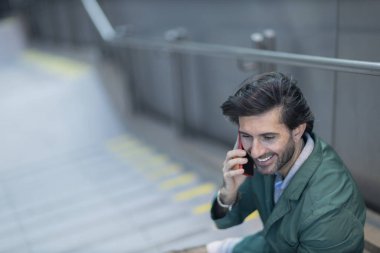 Arka planda bulanık bir manzara olan kapalı alanda akıllı telefon kullanan genç bir adamın görüntüsü. Yüksek kalite fotoğraf. Telefonda konuşuyorlar.. 