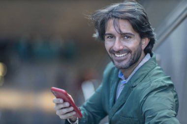 Arka planda bulanık bir manzara olan kapalı alanda akıllı telefon kullanan genç bir adamın görüntüsü. Yüksek kalite fotoğraf. Telefondaki mesajlaşma.. 