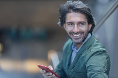 Arka planda bulanık bir manzara olan kapalı alanda akıllı telefon kullanan genç bir adamın görüntüsü. Yüksek kalite fotoğraf. Telefondaki mesajlaşma.. 