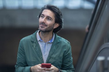 Alacakaranlıkta arka planda bulanık bir manzara olan kapalı bir alanda akıllı telefon kullanan genç bir adamın görüntüsü. Yüksek kalite fotoğraf. Telefonda mesajlaşıyoruz. Gece vakti şehir manzaralı akıllı telefon kullanan genç bir adamın görüntüsü.