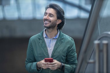 Alacakaranlıkta arka planda bulanık bir manzara olan kapalı bir alanda akıllı telefon kullanan genç bir adamın görüntüsü. Yüksek kalite fotoğraf. Telefonda mesajlaşıyoruz. Gece vakti şehir manzaralı akıllı telefon kullanan genç bir adamın görüntüsü.