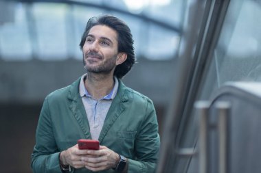 Alacakaranlıkta arka planda bulanık bir manzara olan kapalı bir alanda akıllı telefon kullanan genç bir adamın görüntüsü. Yüksek kalite fotoğraf. Telefonda mesajlaşıyoruz. Gece vakti şehir manzaralı akıllı telefon kullanan genç bir adamın görüntüsü.