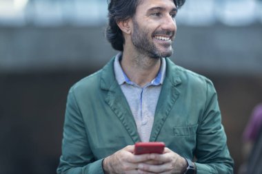 Alacakaranlıkta arka planda bulanık bir manzara olan kapalı bir alanda akıllı telefon kullanan genç bir adamın görüntüsü. Yüksek kalite fotoğraf. Telefonda mesajlaşıyoruz. Gece vakti şehir manzaralı akıllı telefon kullanan genç bir adamın görüntüsü.