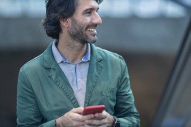 Alacakaranlıkta arka planda bulanık bir manzara olan kapalı bir alanda akıllı telefon kullanan genç bir adamın görüntüsü. Yüksek kalite fotoğraf. Telefonda mesajlaşıyoruz. Gece vakti şehir manzaralı akıllı telefon kullanan genç bir adamın görüntüsü.