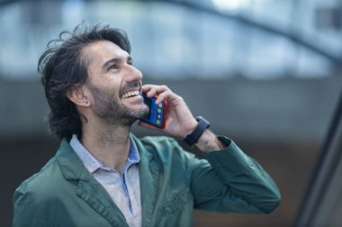 Alacakaranlıkta arka planda bulanık bir manzara olan kapalı bir alanda akıllı telefon kullanan genç bir adamın görüntüsü. Yüksek kalite fotoğraf. Telefonla konuşuyorum. Gece vakti şehir manzaralı akıllı telefon kullanan genç bir adamın görüntüsü.
