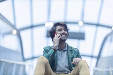 Arka planda bulanık bir manzara olan kapalı alanda akıllı telefon kullanan genç bir adamın görüntüsü. Yüksek kalite fotoğraf. Telefonda konuşuyorlar.. 