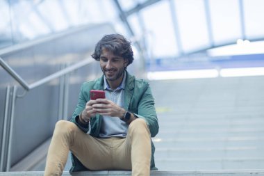 View of young man using a smartphone at indoor space with a blurred view landscape in the background. High quality photo. Texting on the phone.  clipart