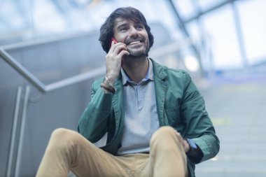 Arka planda bulanık bir manzara olan kapalı alanda akıllı telefon kullanan genç bir adamın görüntüsü. Yüksek kalite fotoğraf. Telefonda konuşuyorlar.. 