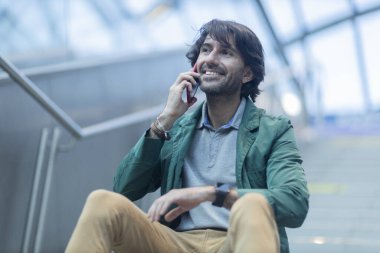 Arka planda bulanık bir manzara olan kapalı alanda akıllı telefon kullanan genç bir adamın görüntüsü. Yüksek kalite fotoğraf. Telefonda konuşuyorlar.. 