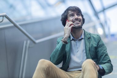 Arka planda bulanık bir manzara olan kapalı alanda akıllı telefon kullanan genç bir adamın görüntüsü. Yüksek kalite fotoğraf. Telefonda konuşuyorlar.. 