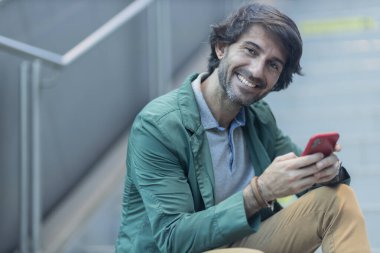 Arka planda bulanık bir manzara olan kapalı alanda akıllı telefon kullanan genç bir adamın görüntüsü. Yüksek kalite fotoğraf. Telefondaki mesajlaşma.. 