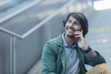 Arka planda bulanık bir manzara olan kapalı alanda akıllı telefon kullanan genç bir adamın görüntüsü. Yüksek kalite fotoğraf. Telefonda konuşuyorlar.. 